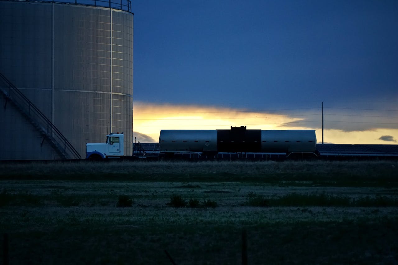 A white truck parked by a large silo in a rural field at sunset. Tranquil countryside scene.