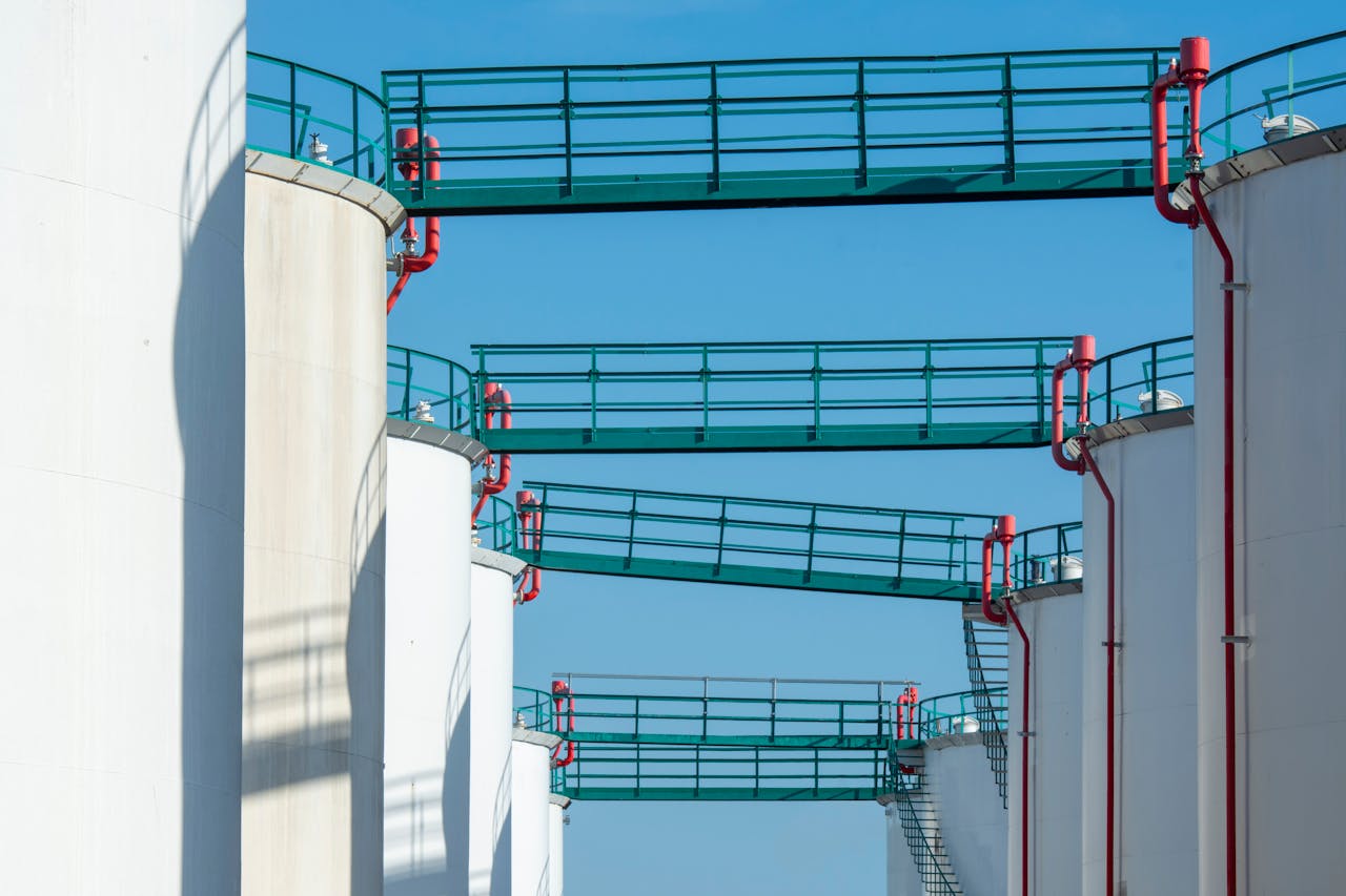 Modern industrial storage tanks with walkways against a clear blue sky.